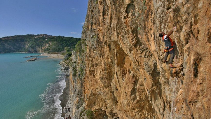 uno scalatore su una rossa parete verticale a picco sul mare