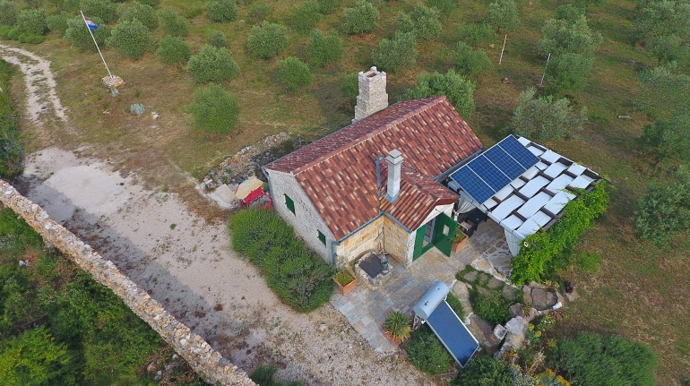 Vista aerea sulla casa, visibili il camino, i pannelli solari, l'impianto per il riscaldamento dell'acqua, il pozzo, la tettoia e gli ulivi
