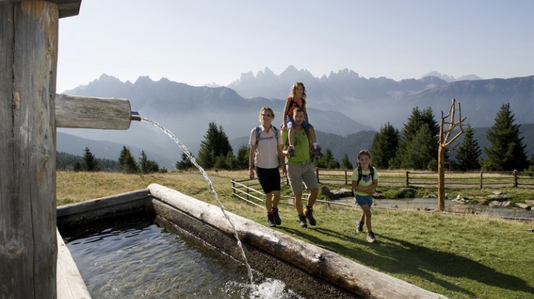 Immagine di una famiglia, che passeggia su un prato verde, in montagna, vicino ad una fonte d'acqua