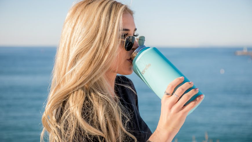 Ragazza che beve da una bottiglia termica, per diventare un viaggiatore sostenibile