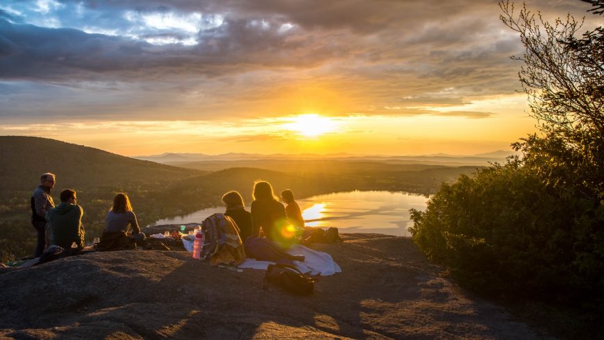 Un piccolo gruppo di persone sedute in cima a una montagna che guarda il tramonto in lontananza.
