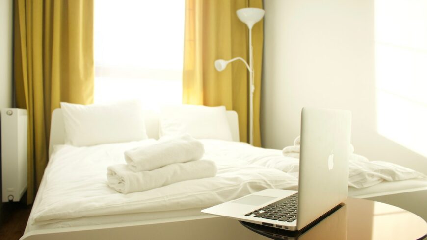 Un letto con lenzuola bianche e asciugamani; un computer portatile su un tavolo
