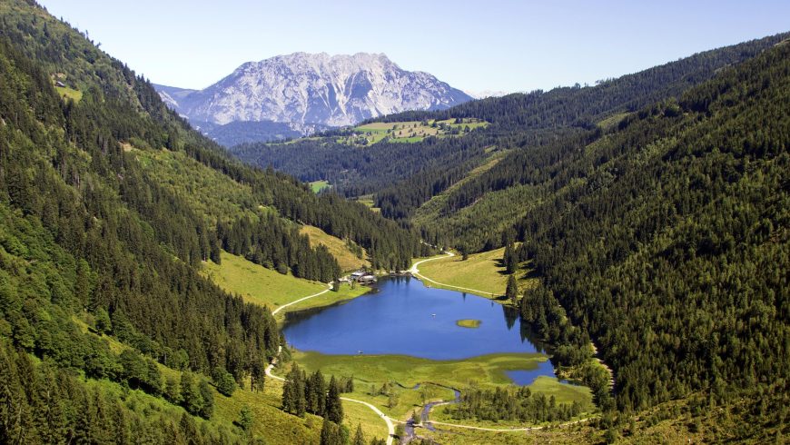 Lago circondato da montagne verde e una montagna innevata sullo sfondo