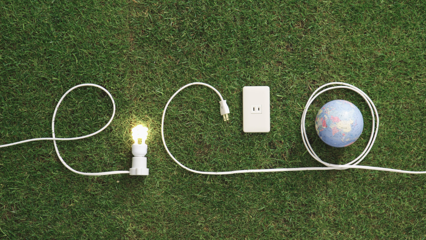 Lampadina e prese elettriche su prato verde che formano la parola “eco” con il pianeta Terra, simbolo di energia sostenibile e ambiente.