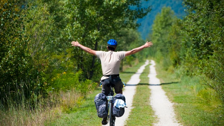 Viaggiatore in bici su percorso ciclabile immerso nel verde