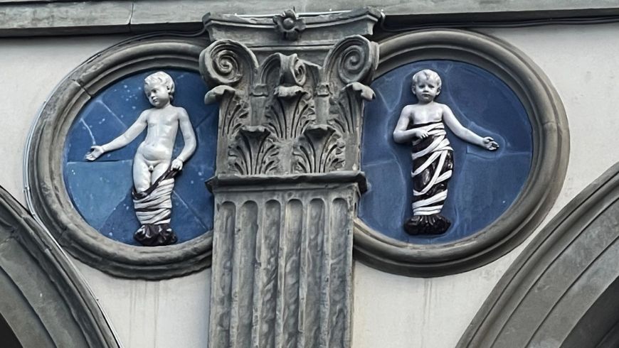 Dettaglio della facciata dell’Ospedale degli Innocenti a Firenze, con capitello e putti in bassorilievo su fondo blu.