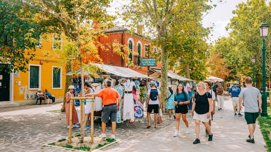 una scena di mercato, con edifici colorati e persone che fanno acquisti in estate