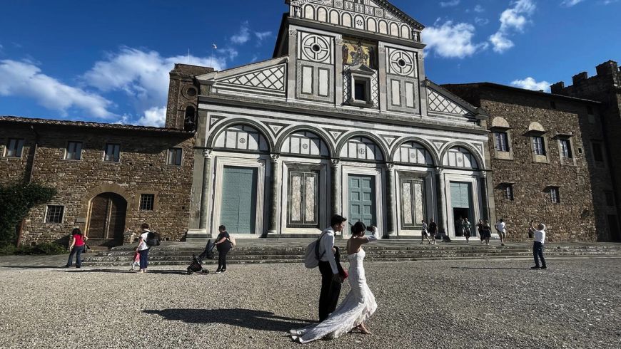 Facciata geometrica in marmo bianco e verde della Basilica di San Miniato al Monte a Firenze, con una coppia di sposi davanti all'ingresso.