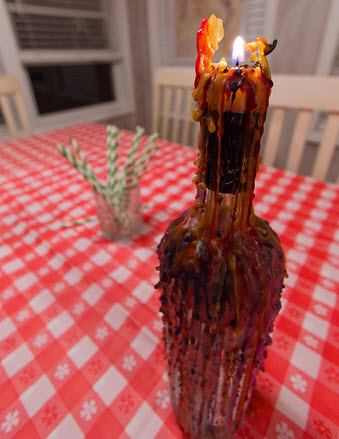 Wax candle with a burning flame at the top of an empty bottle