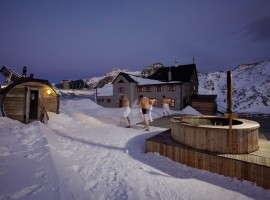 in a snowy landscape, three men are going to the refuge; on the left, there is the swedish sauna, on the right the heated pool (Refuge Bella Vista, BO)