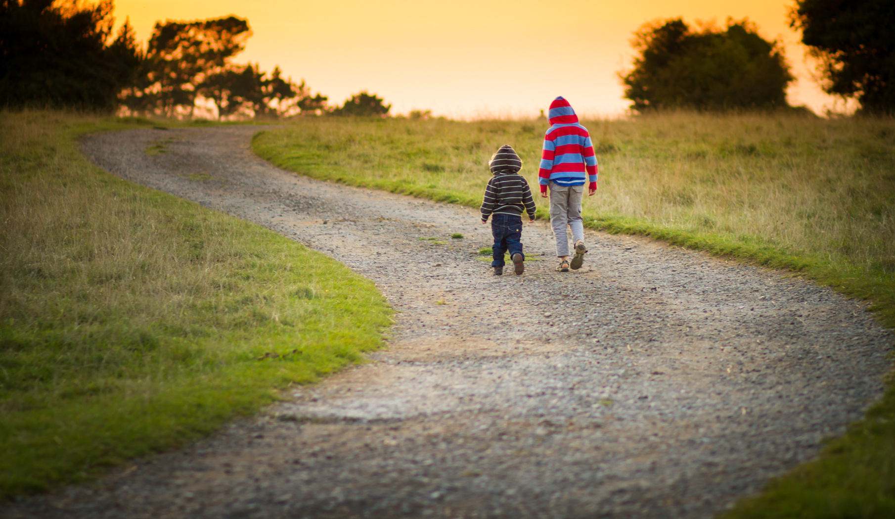 two young boys walking together down a path towards the setting sun