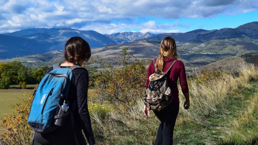 Two girls hiking in the mountains with lightweight backpacks, surrounded by beautiful natural scenery.
