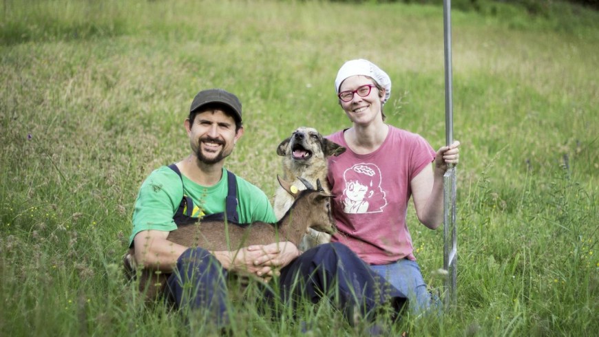 the owners of the farmhouse with one of their goats and a dog sitted in the meadow