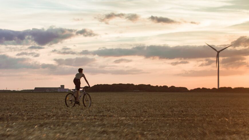A person on a bicycle in a field by a wind turbine