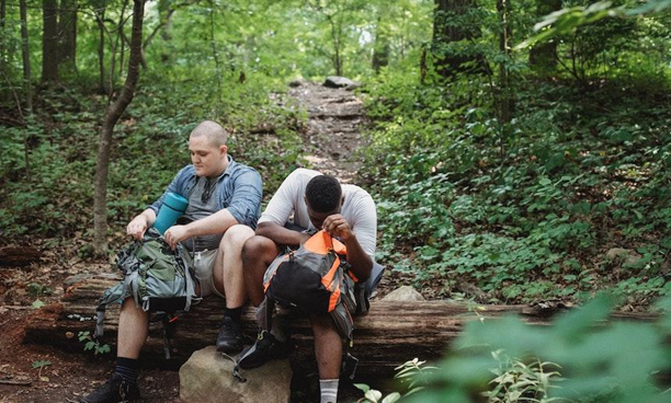 Two male friends resting on a log in the forest. 