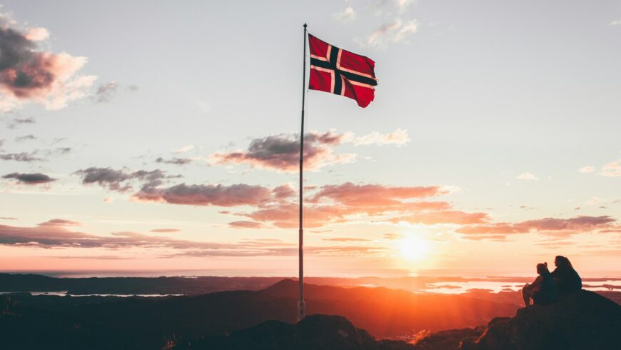 Norway flag on a pole, sunset in the background.
