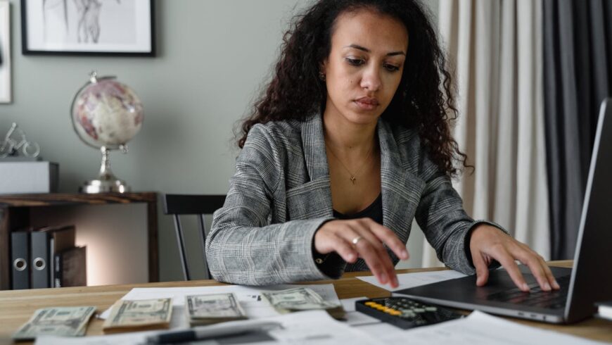 A woman using a calculator and a laptop to count money and pay bills