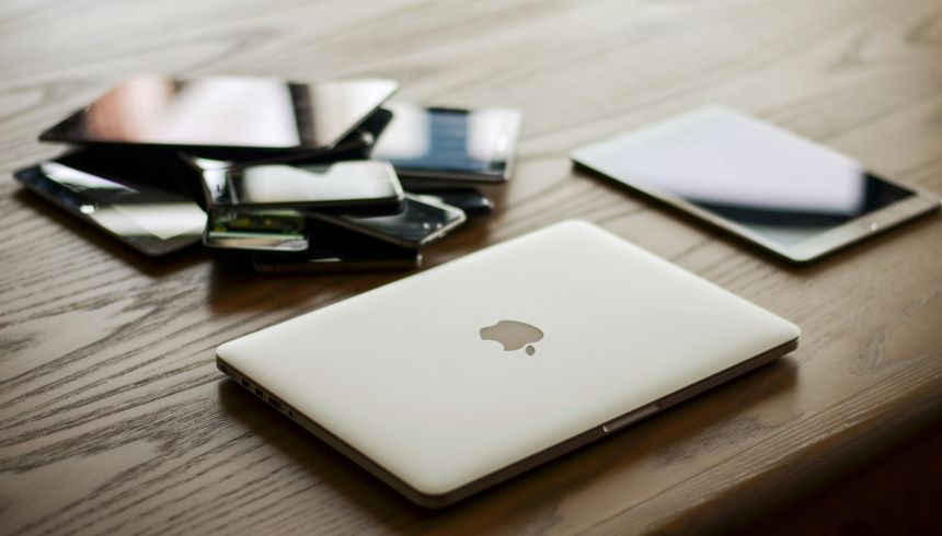 A collection of old smartphones, tablets, and laptops on a wooden table, representing the importance of reducing electronic waste.