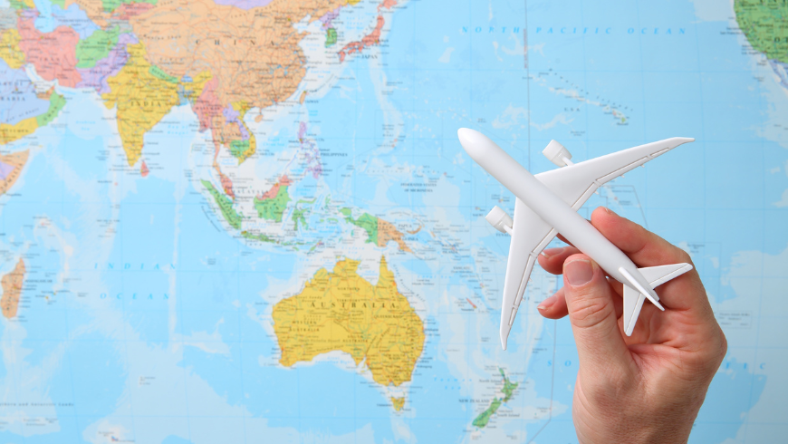 Hand Holding a Model Airplane Over a Map of Asia and Australia