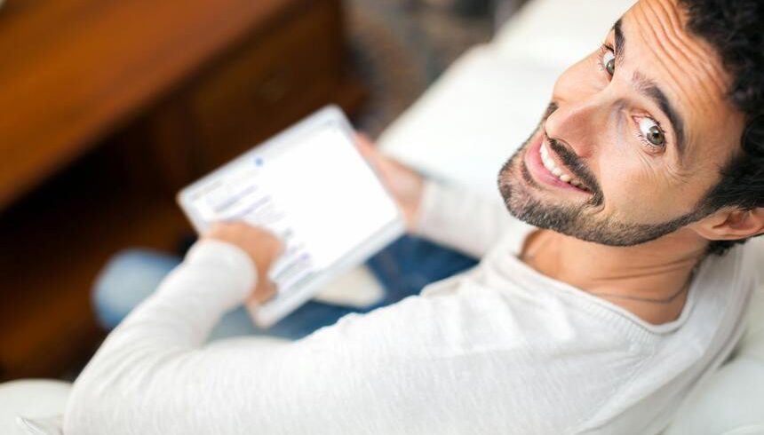 A smiling person using a tablet on a couch.