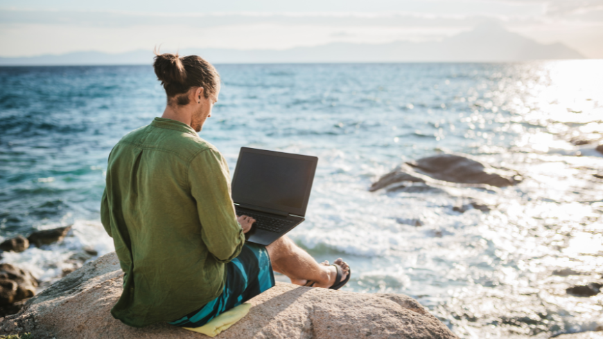 Digital nomad working on a laptop while overlooking the sea, enjoying a sustainable and scenic work environment
