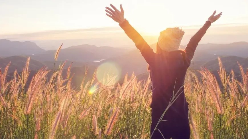 A person stands with raised arms in a field at sunset – expressing freedom, well-being, and the positive impact of sustainable experiences.