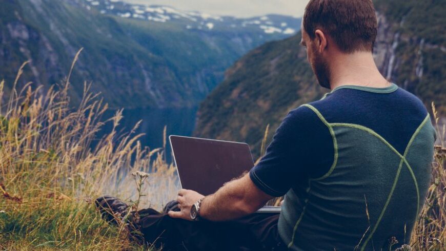 Remote worker using a laptop in mountain, combining sustainable travel with flexible working