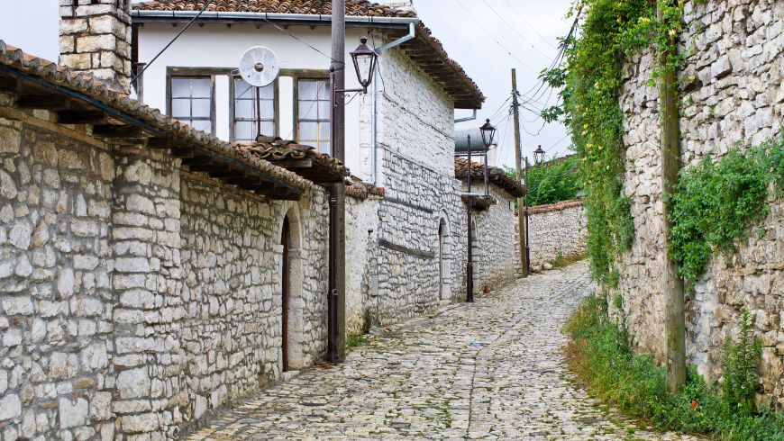 Narrow cobbled alley lined with traditional white Ottoman houses in the historic old town of Berat, Albania.