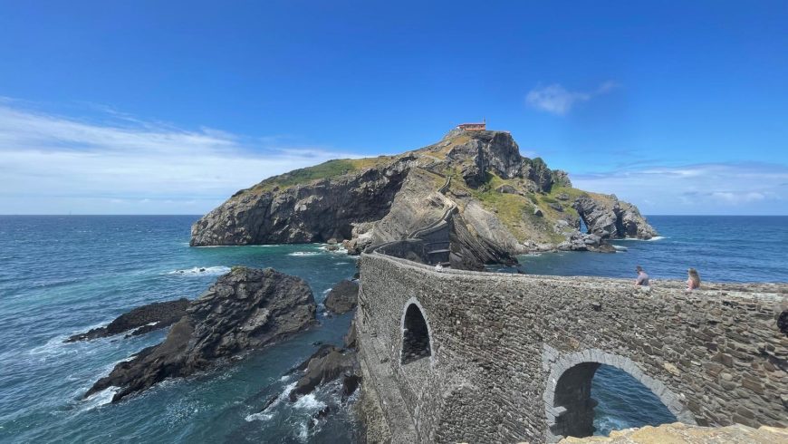 the Hermitage of San Juan de Gaztelugatxe with the stone bridge in the foreground and two people crossing it