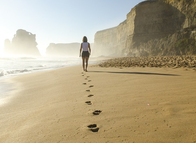 Woman walking barefoot on a beach, leaving footprints in the sand