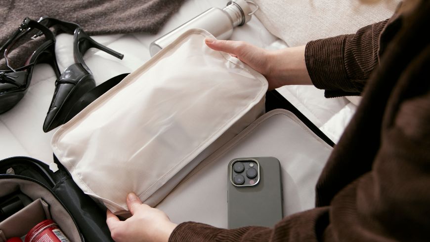 Young woman packing a suitcase, with packing cubes, a reusable water bottle, and a smartphone in the foreground.