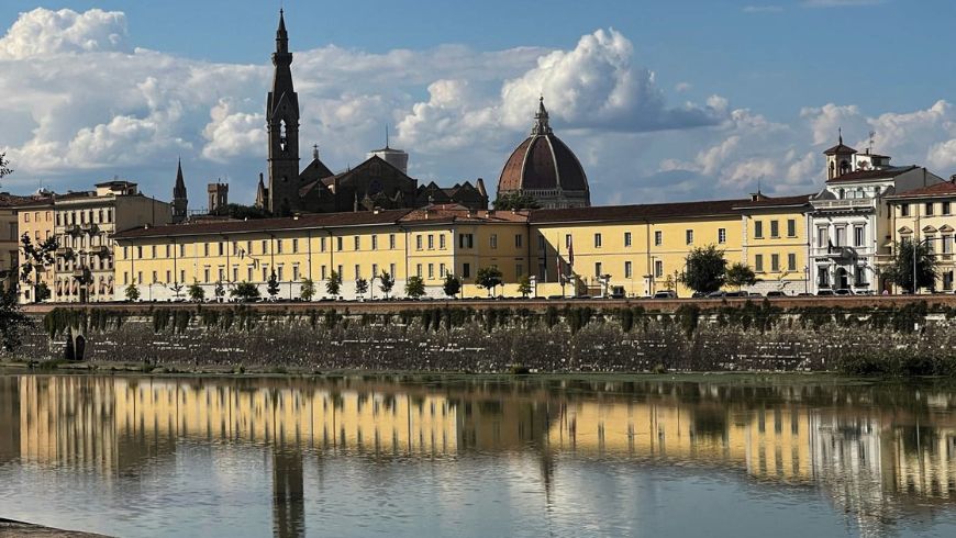 Cycling along the Arno in Florence, with historic buildings reflected in the water.