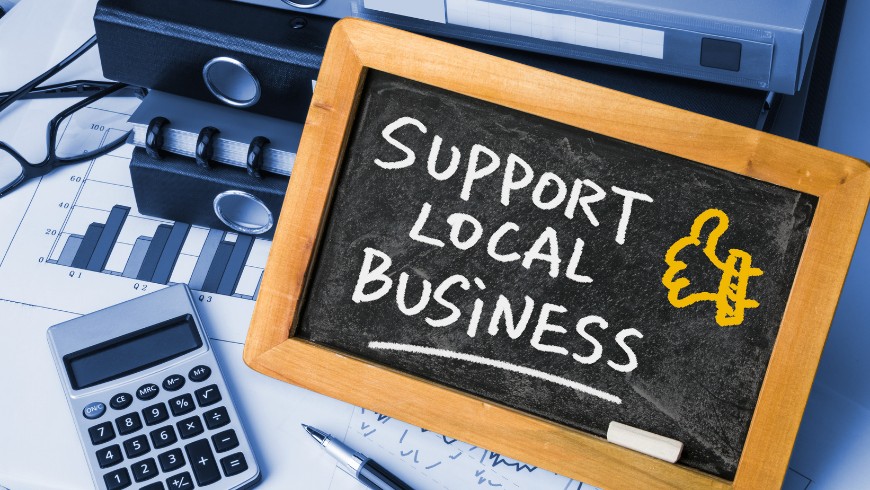eine kleine Tafel mit der Aufschrift „Support Local Business“, die auf einem Schreibtisch steht. Sie symbolisiert die Bedeutung der Unterstützung lokaler Unternehmen und einer nachhaltigen, regionalen Wirtschaft.