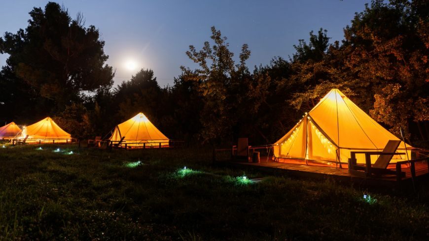 Drei leuchtende Bell-Zelte auf einem Glamping-Platz bei Nacht unter einem Vollmond, umgeben von Bäumen.