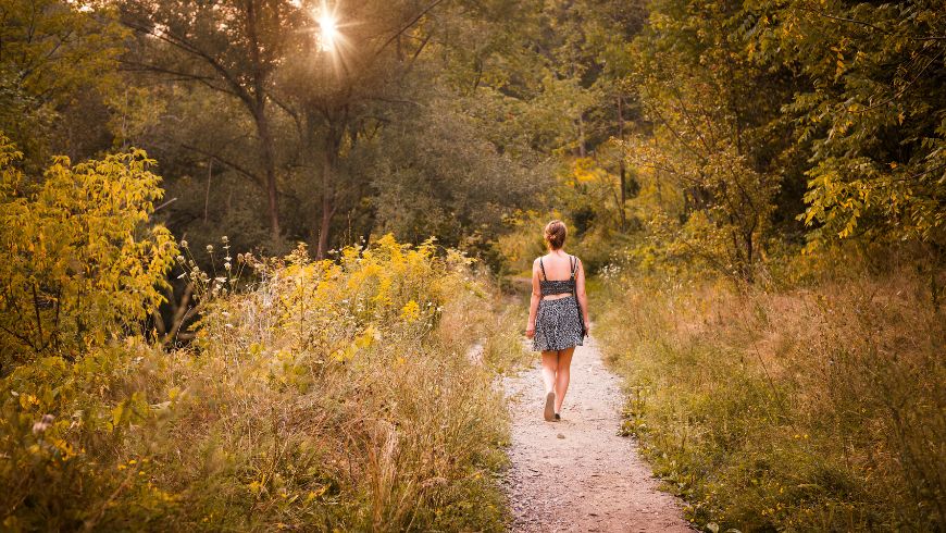 Eine Person spaziert auf einem schmalen Naturpfad durch eine sonnendurchflutete Landschaft – ein Symbol für nachhaltige Erlebnisse und bewusstes Reisen im Einklang mit der Natur.