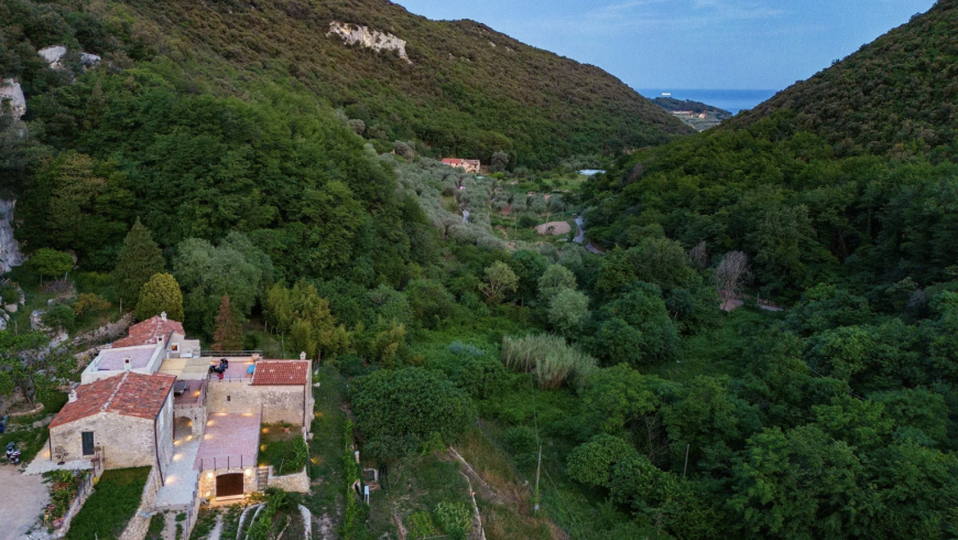 Blick von oben auf Ca' del Buio, den grünen Wald, der sie umgibt, und das Meer in der Ferne