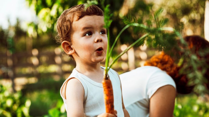 Glückliches Kind mit einer Karotte aus dem Garten
