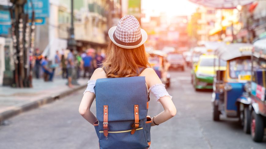 Eine Reisende erkundet zu Fuß eine neue Stadt mit leichtem Gepäck und nutzt ihr Smartphone zur Navigation und für den Zugang zu digitalen Reiseinformationen.