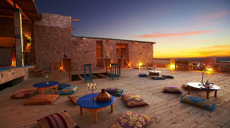 Ecohotel Ane Vert, en Marruecos. Espacio abierto con pequeñas mesas azules y almohadas arabes 