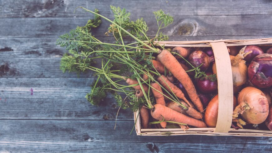 Un cestino con verdure organiche come carote e cipolle.