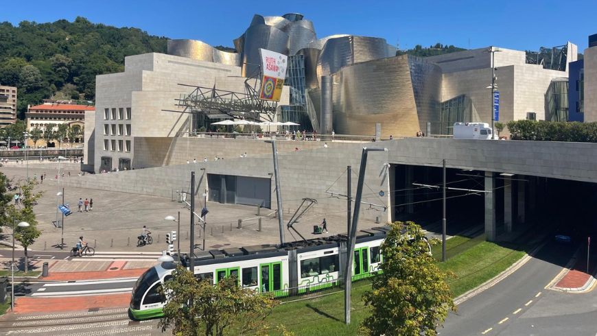 Metro de Bilbao atravesando una zona verde con el Guggenheim al fondo.