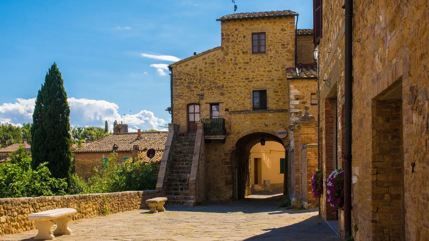 Rue du village en pierre de San Quirico d’Orcia, avec bâtiments traditionnels et ciel bleu.