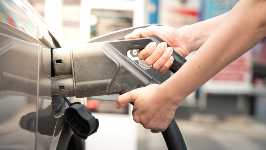 Personne en train de faire le plein de carburant sur une station-service, illustrant le contraste avec une borne de recharge rapide pour voiture électrique (CCS).