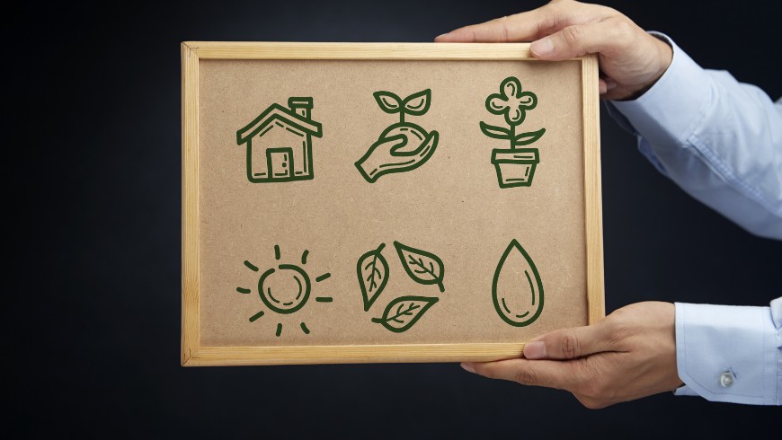 avantages hébergement écoresponsable : personne tenant un panneau avec des symboles liés à l’écologie, comme une maison, des plantes, le soleil, des feuilles et une goutte d’eau. Ces éléments représentent un mode de vie durable, les énergies renouvelables et le tourisme responsable.